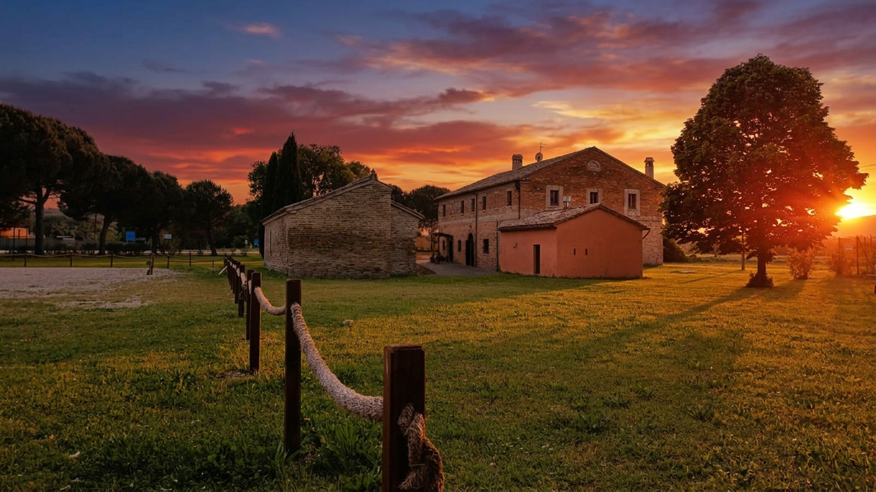 Il casale de La Pampa al tramonto, con prato verde, alberi e cielo infuocato